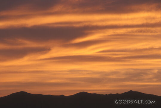 A cloudy orange sky about black mountains.