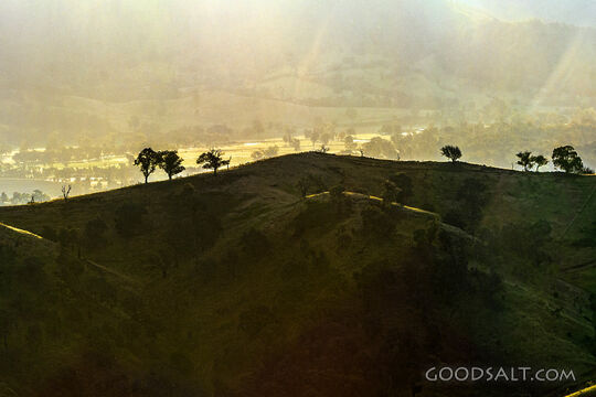 golden late sun bathes country scene and hillsides in misty light.