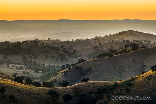 golden late sun bathes country scene and hillsides in misty light.
