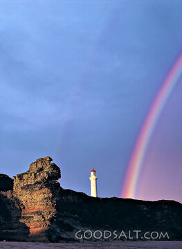 rock formation with rainbow and lighthouse