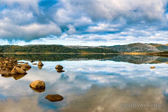 Rocky shoreline mirrored in alpine lake.