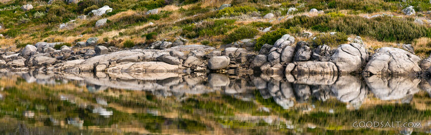 Rocky shoreline mirrored in alpine lake.