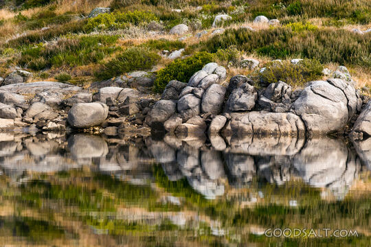 Rocky shoreline mirrored in alpine lake.