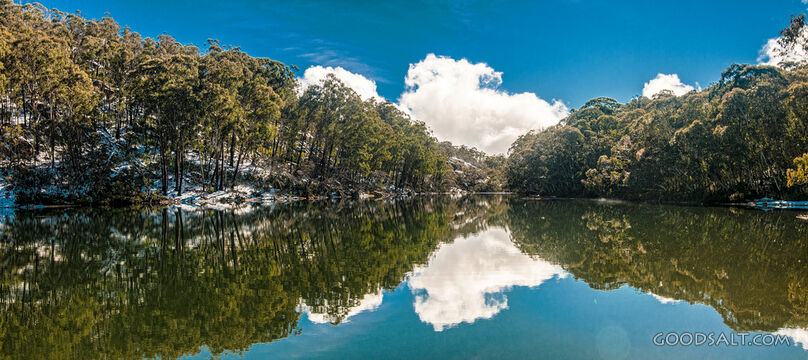 Snow and trees on the other side of a lake are reflected in its waters.