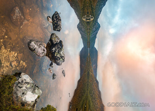 Still reflective lake with foreground boulders at sunrise.