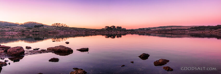 Sunrise over mirror water and rocks of alpine lake.