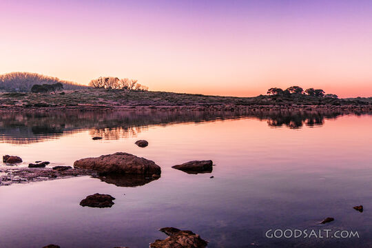 Sunrise over mirror water and rocks of alpine lake.