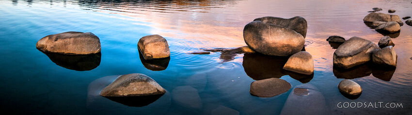 Sunrise over mirror water and rocks of alpine lake.