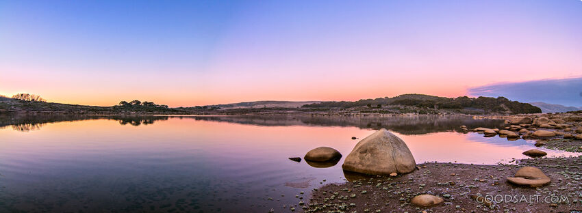 Sunrise over mirror water and rocks of alpine lake.