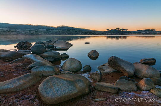 Sunrise over mirror water and rocks of alpine lake.