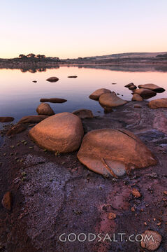Sunrise over mirror water and rocks of alpine lake.