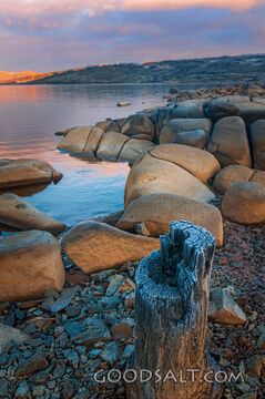 Sunrise over mirror water and rocks of alpine lake.