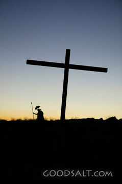 A silhouette of a cross with a soldier in the distance.