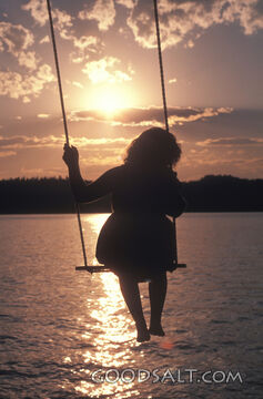 A little girl swinging over a sparkling ocean.