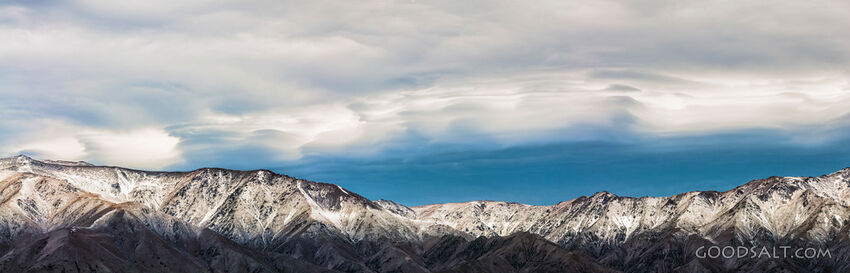 Dramatic stormy Lenticular clouds sit above snowy mountains.