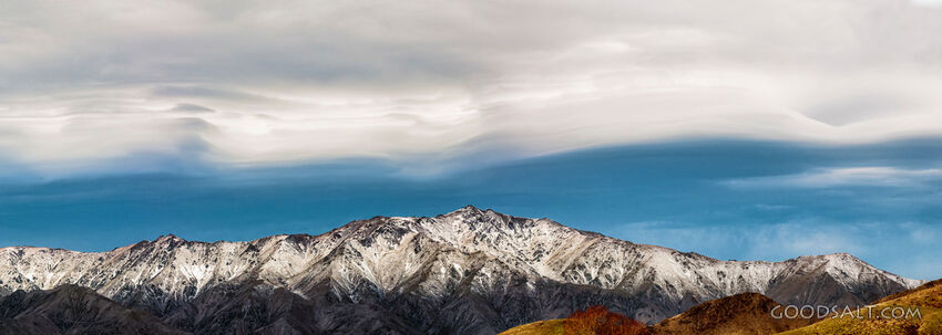 Dramatic stormy Lenticular clouds sit above snowy mountains.