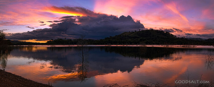 Dramatic sunset and storm cloud over still lake waters.