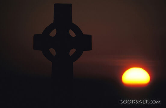 The silhouette of a cross in front of a bright sunset.