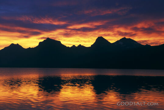 A fiery sunset behind large mountains and a body of water.