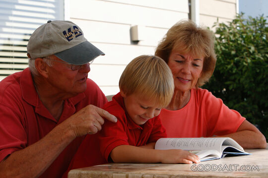 Man and woman reading to little boy on patio.