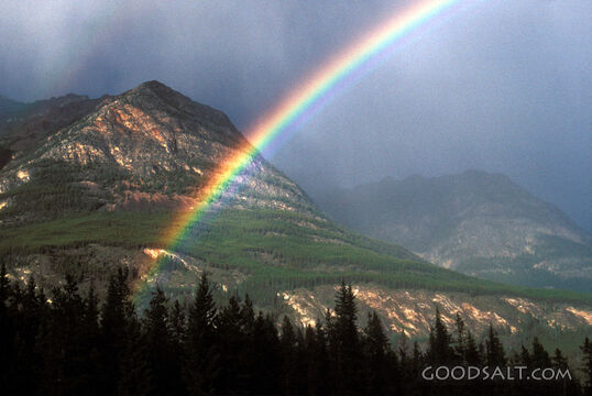 A bright rainbow in front of a tall mountain.