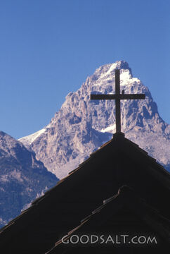 Cross on top of building silhouetted by mountain peak.