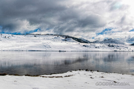 Snow covered surronds and freezing water of alpine lake.