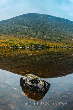 Still reflective lake with foreground boulders at sunrise.