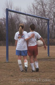 Two girls from different teams, walking together on soccer field 