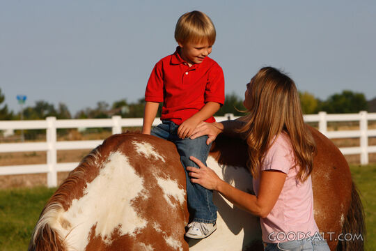 Woman smiling up at little boy on horseback.