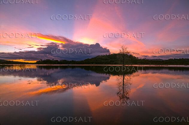 Dramatic sunset and storm cloud over still lake waters.