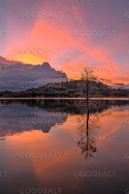 Dramatic sunset and storm cloud over still lake waters.