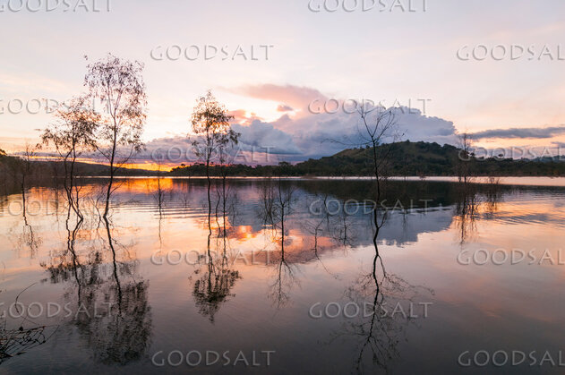 Dramatic sunset and storm cloud over still lake waters.