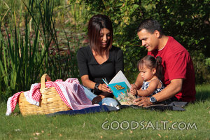 Happy family picnicing in park, reading storybook.