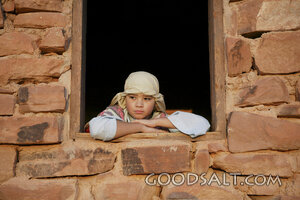 child in costume in a window of a stone house resting his arms on the window sill