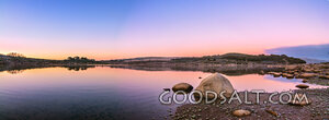 Sunrise over mirror water and rocks of alpine lake.