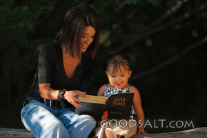 Woman reading Bible to little girl outdoors in summer.