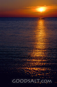 A Small Boat Sailing Through the Ocean With a Sun Setting In