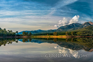 Dramatic sky over large mountain reflected in waters of lake.