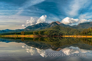 Dramatic sky over large mountain reflected in waters of lake.