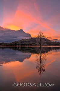 Dramatic sunset and storm cloud over still lake waters.