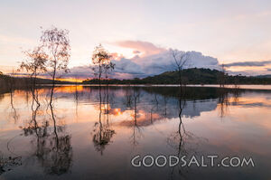 Dramatic sunset and storm cloud over still lake waters.