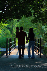 Happy family walking across bridge in park in summer.