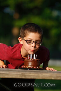 Little boy blowing out birthday candles outdoors in summer.