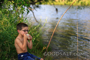 Little boy eating sandwich while fishing in summer.