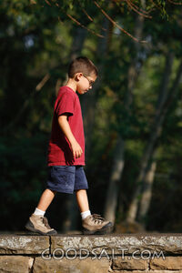 Little boy walking on stone wall in summer.