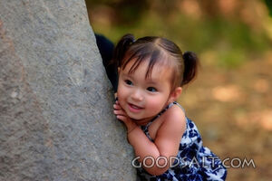 Little girl playing peekaboo around stone wall.
