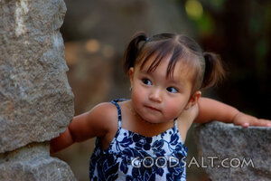 Little girl playing peekaboo around stone wall.
