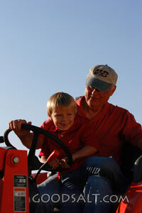 Man and little boy on tractor outdoors in summer.