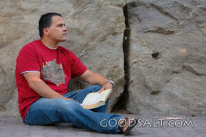 Man reading, leaning against stone wall.